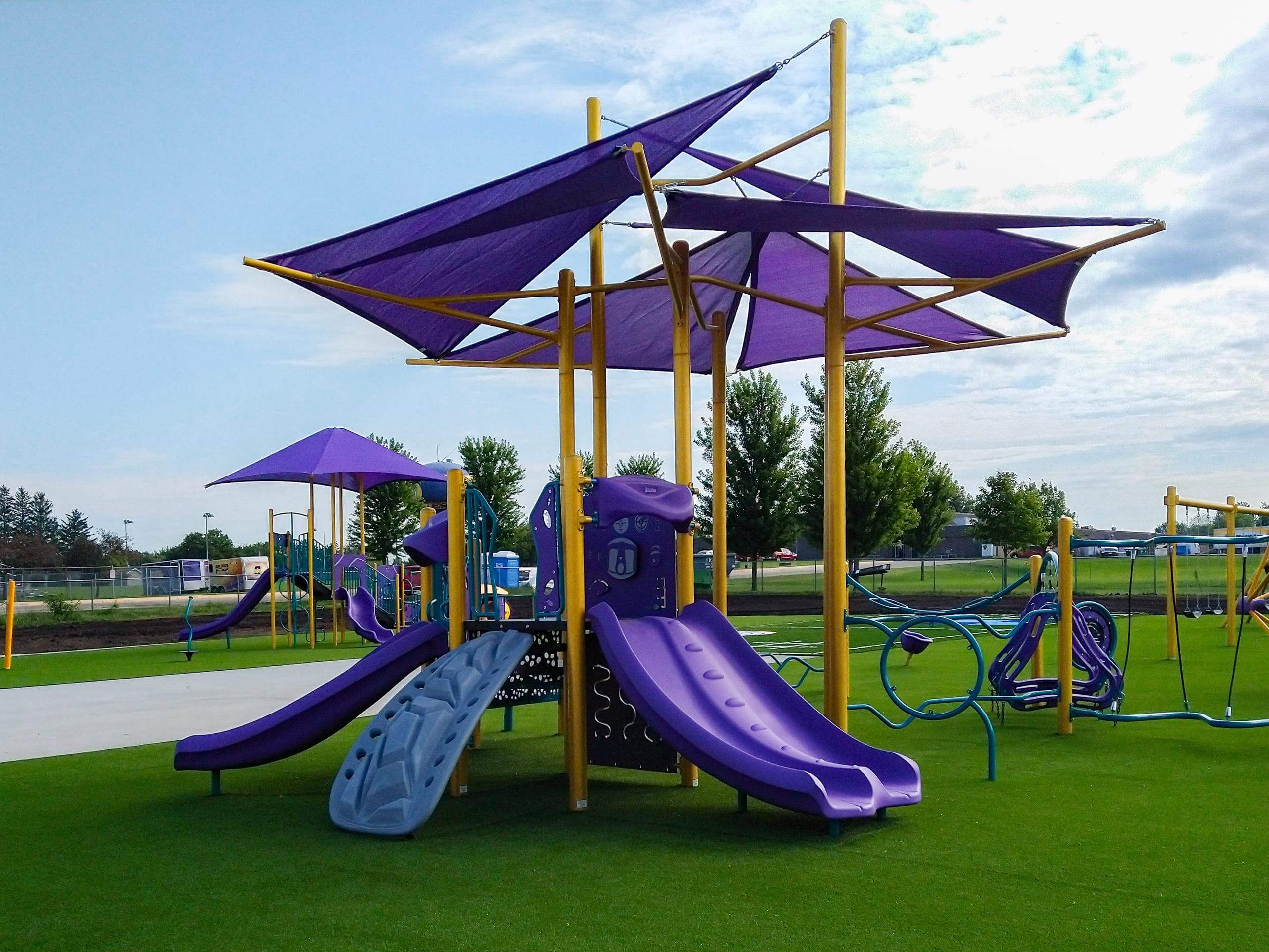 Playground with purple slides and sunshades, and vibrant play panels on green turf.