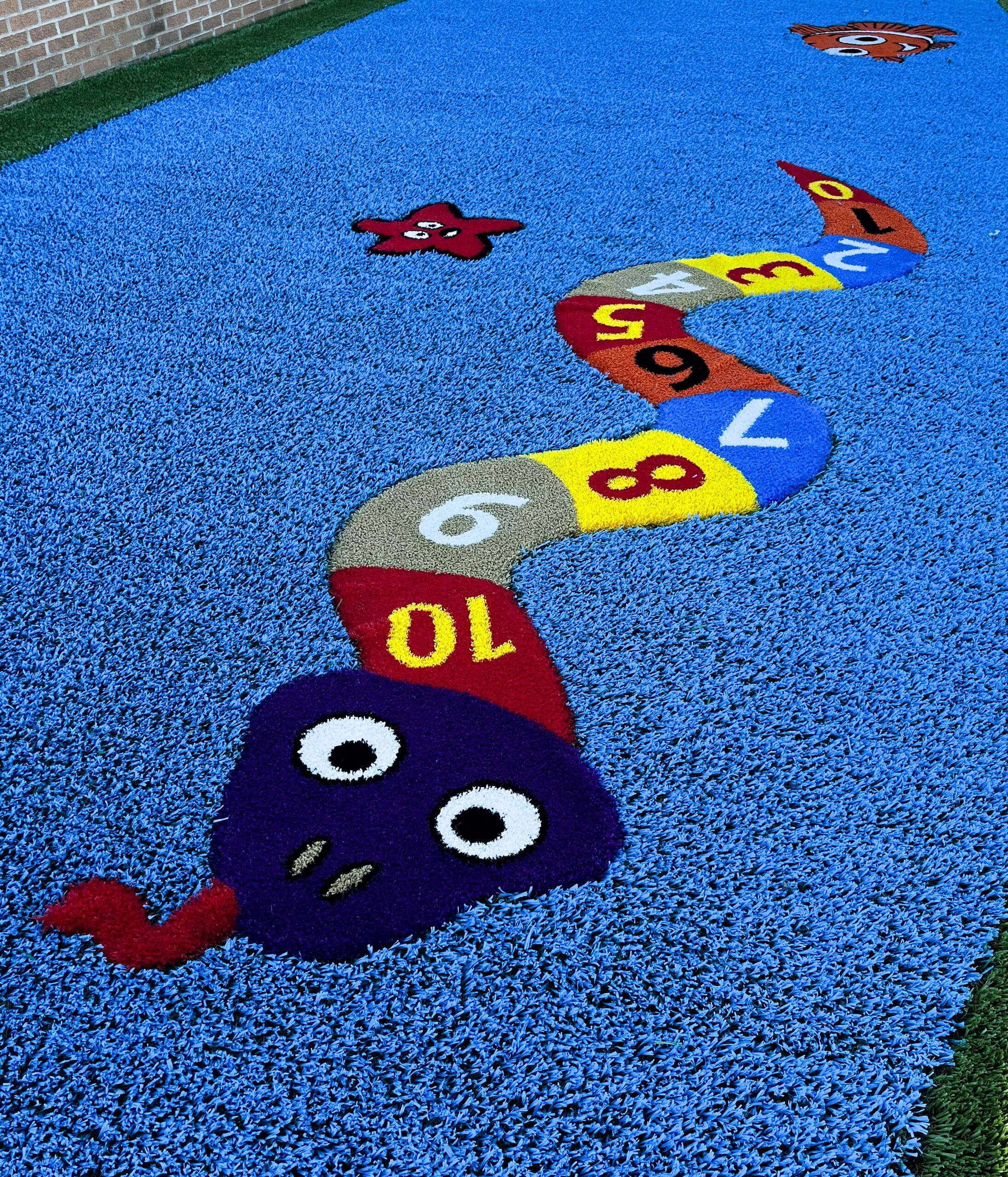 Colorful snake-like 'Funsert' design on blue synthetic playground turf with playful numbers and characters.