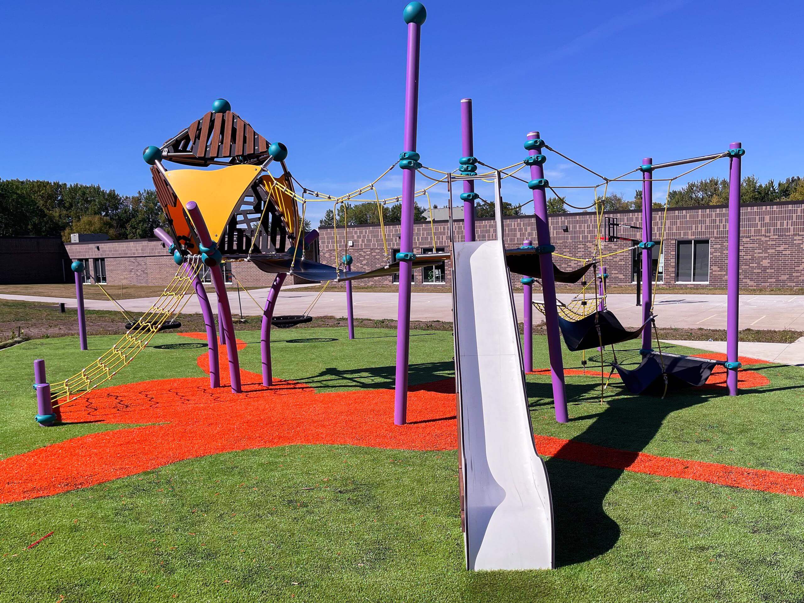 Innovative playground featuring a climbing web, synthetic orange surface, and modern play equipment.