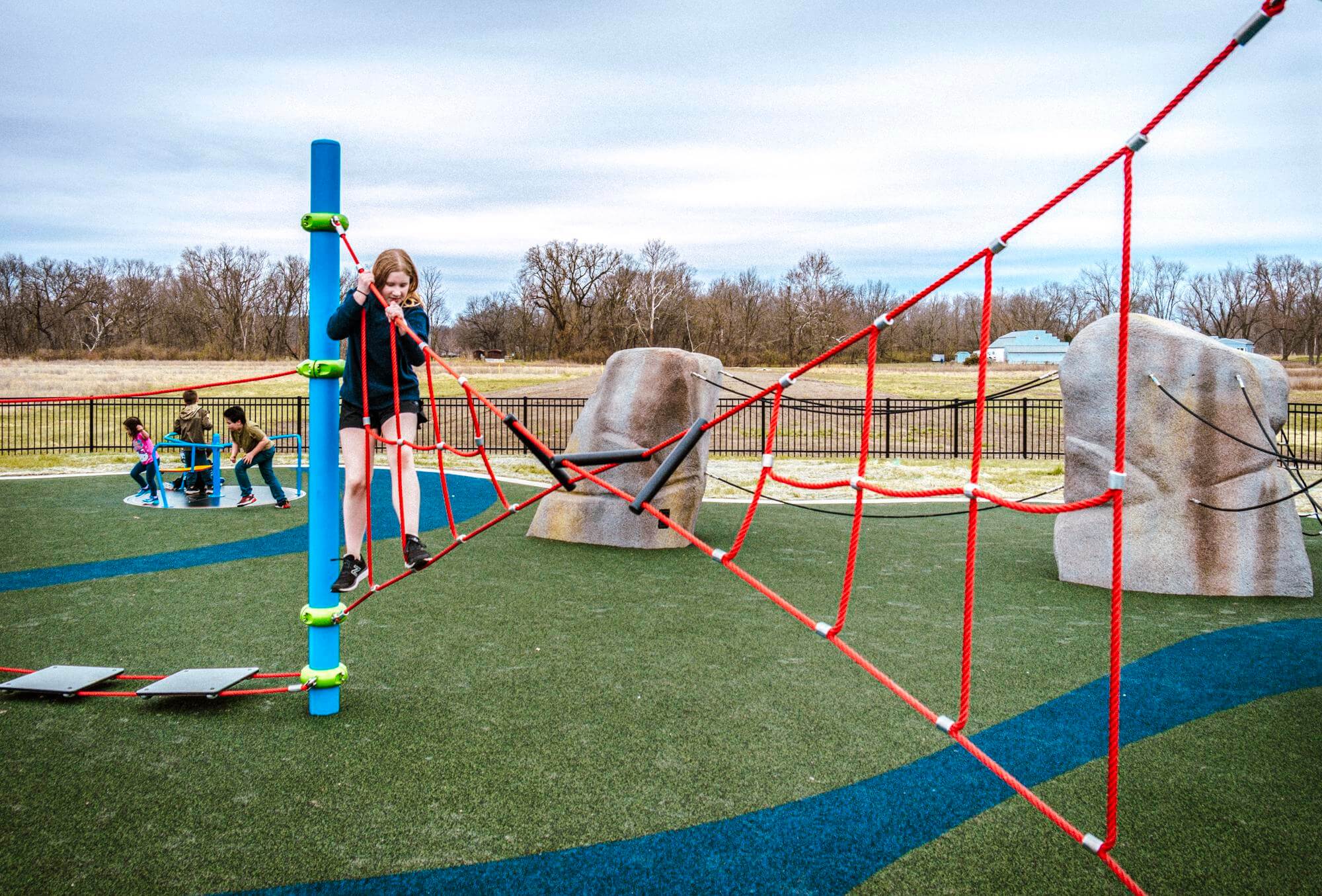 A child in a blue jacket climbing a red rope structure, demonstrating the interactive and challenging elements of the playground.