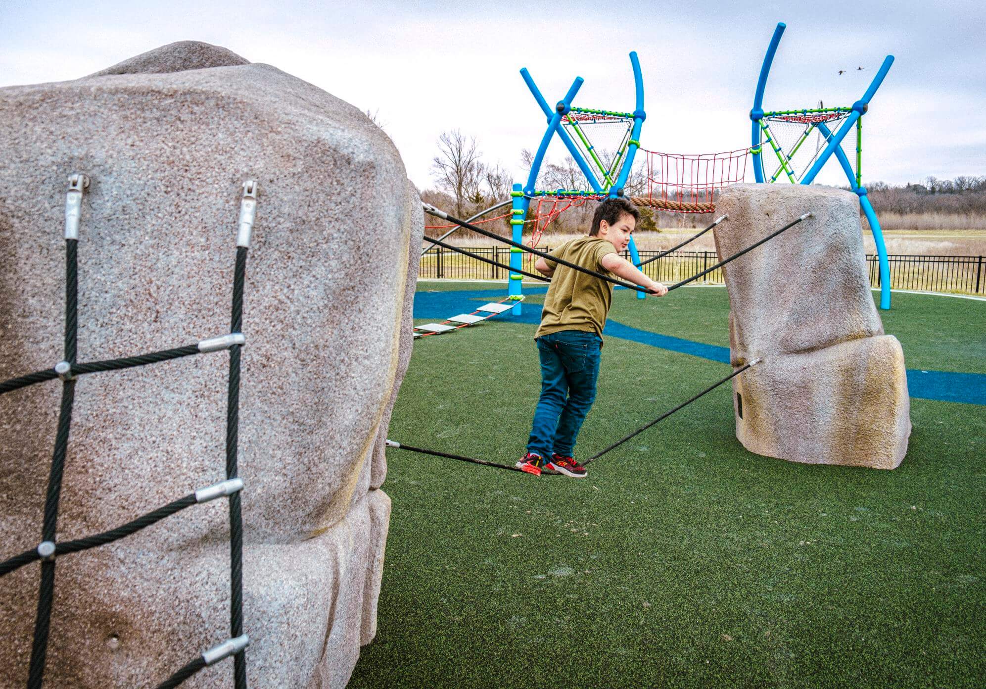 A child engaging with a rope feature connected to sculpted boulders, with complex climbing structures in the background.