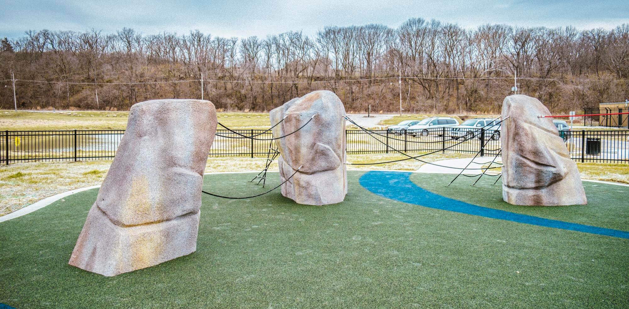 Several artificial climbing boulders with rope features are spread across a playground with a curving blue path on green turf.