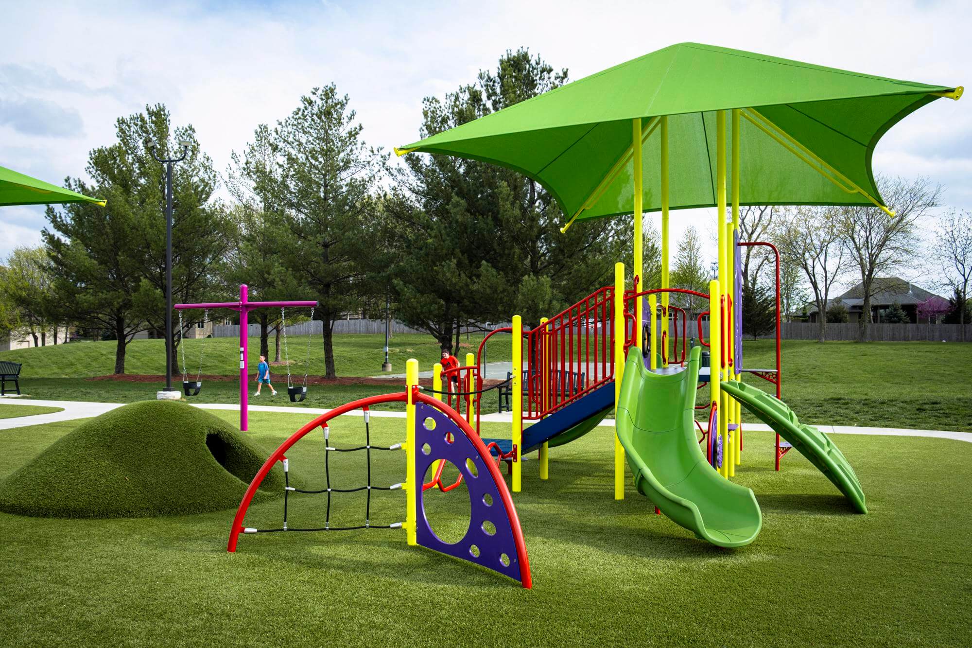 Playground with children on equipment and a dome climber on well-maintained synthetic grass.