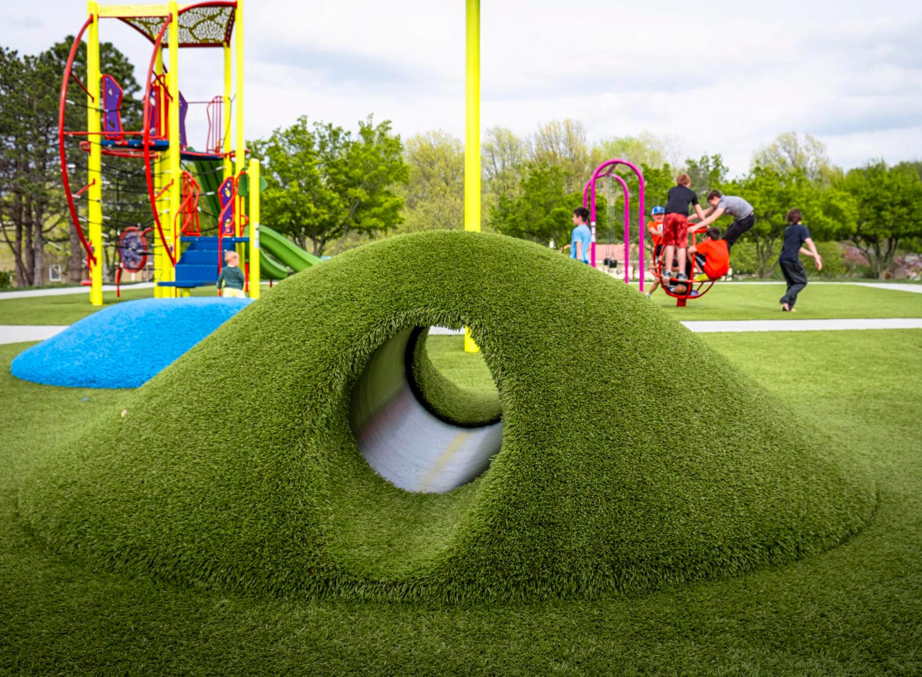 Playground with children on equipment and a dome climber on well-maintained synthetic grass.