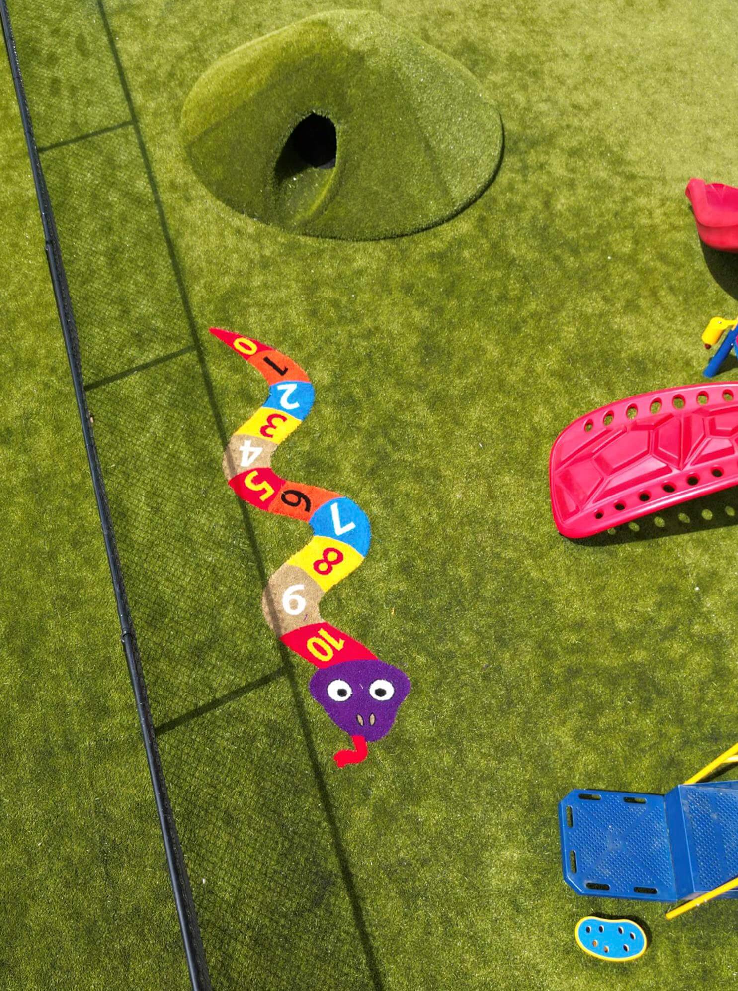 Close-up view of a playground hopscotch path featuring numbers and a cartoon snake design on artificial turf.