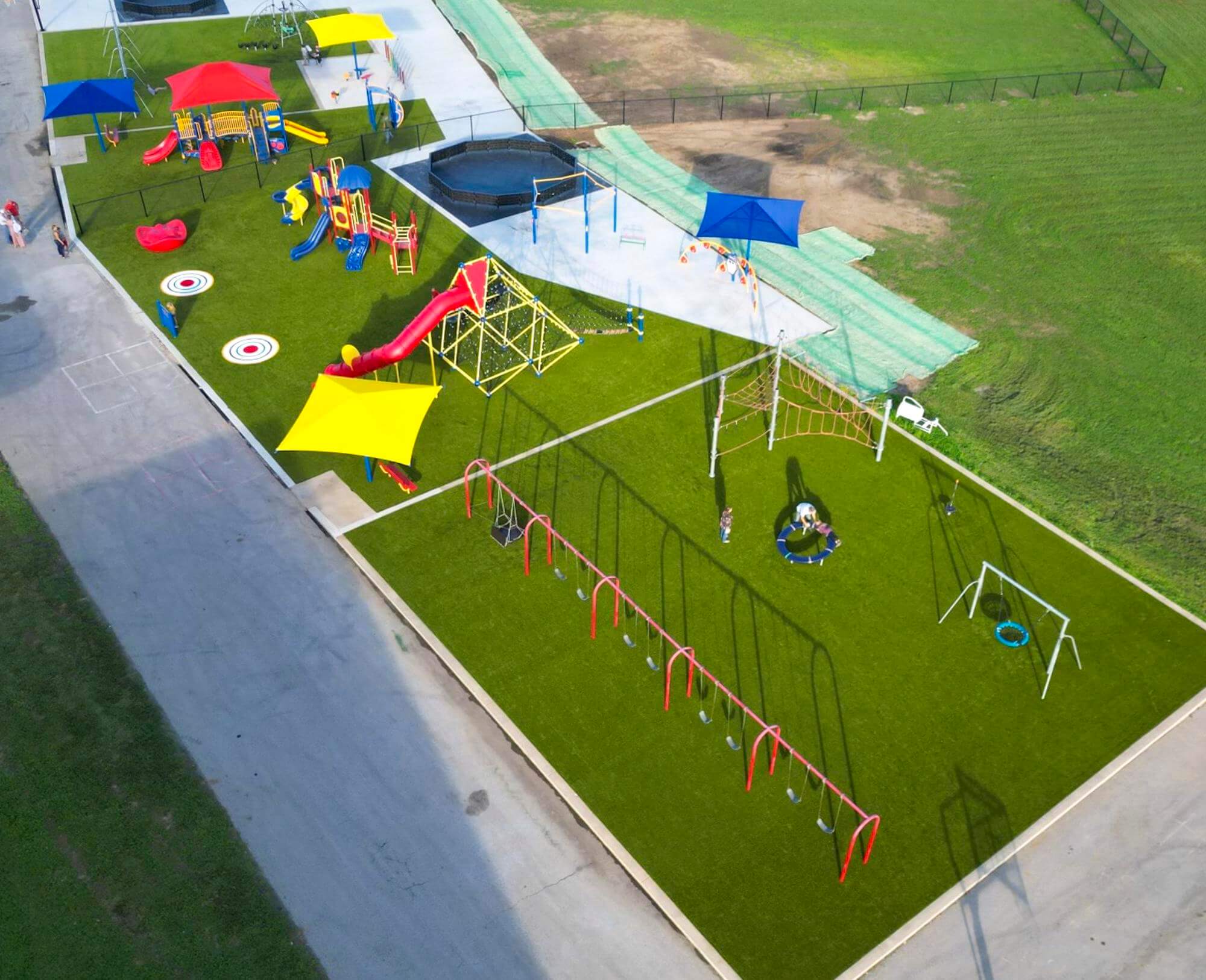 High angle view of a colorful playground with swings, slides, and a climbing net, set within a green artificial turf field.