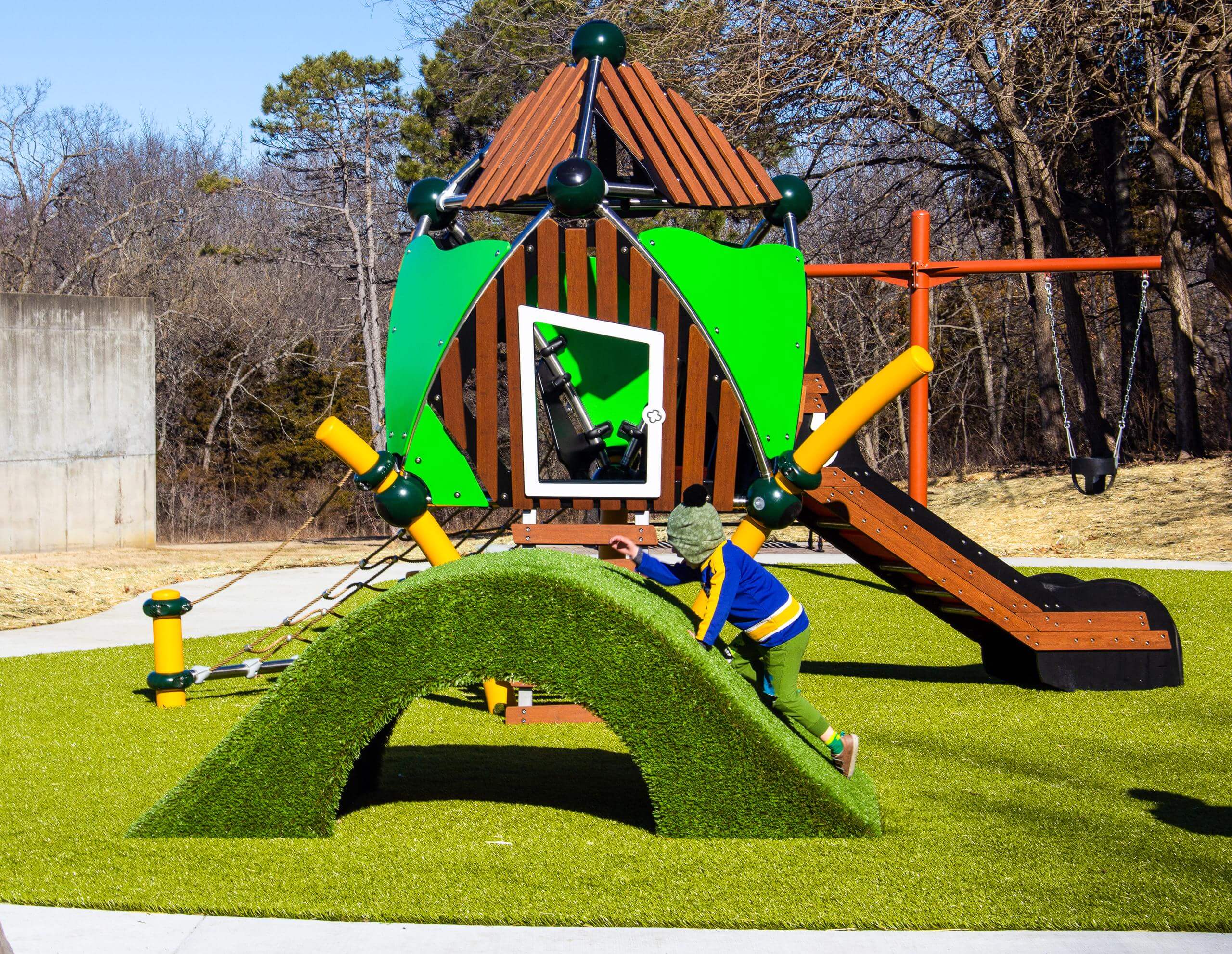 Child climbing on hilly mound with slide and playset in background.