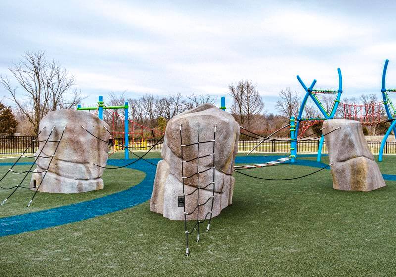 Overview of a playground with sculptural boulders and a complex climbing structure, showcasing a variety of activities for children.
