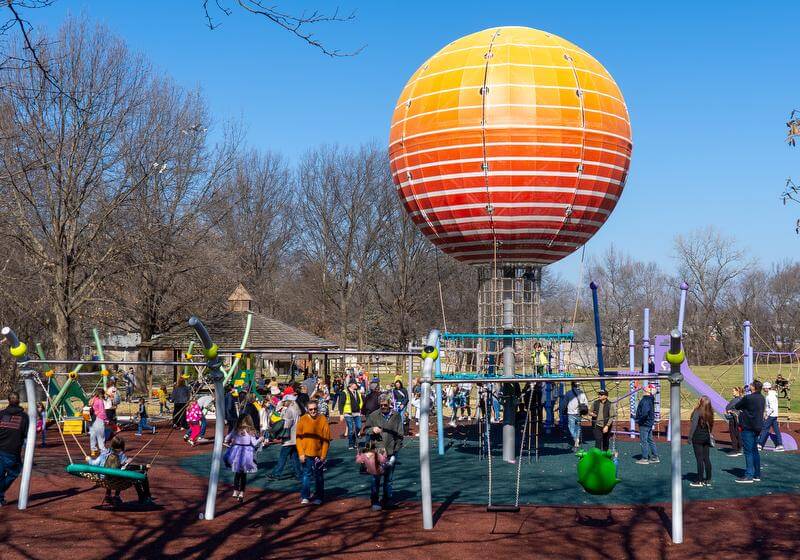 Wide angle view of a playground with swings and extra large balloon structure in the background
