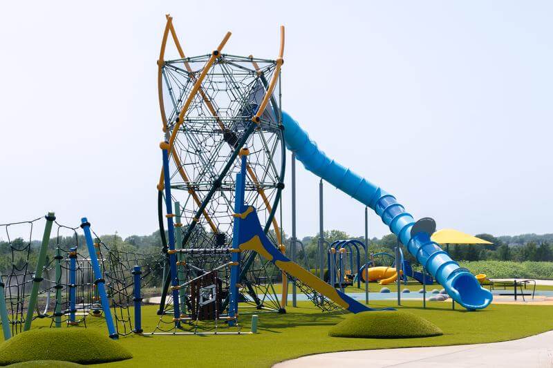 Tall yellow, blue, and green playground structure with green synthetic turf