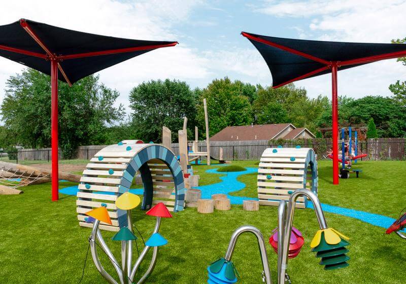 Natural-themed playground at Eudora ELC with shade structures, interactive elements, and musical flowers on turf for early childhood play in Eudora, Kansas.